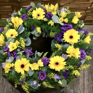 An open wreath in warm and tasteful purples and gold shades. 24 hours notice, or similar design for same day delivery. Due to seasonal variations some items may be substituted to produce a display of equal quality and value.