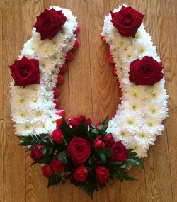 A horse shoe with creams and red rose spray green foliage. 24 hrs notice required Available in colour of your choice. Due to seasonal variations some items may be substituted to produce a display of equal quality and value. Professionally arranged by our expert florists with care. Delivered by hand by our own driver. Click & collect is also available